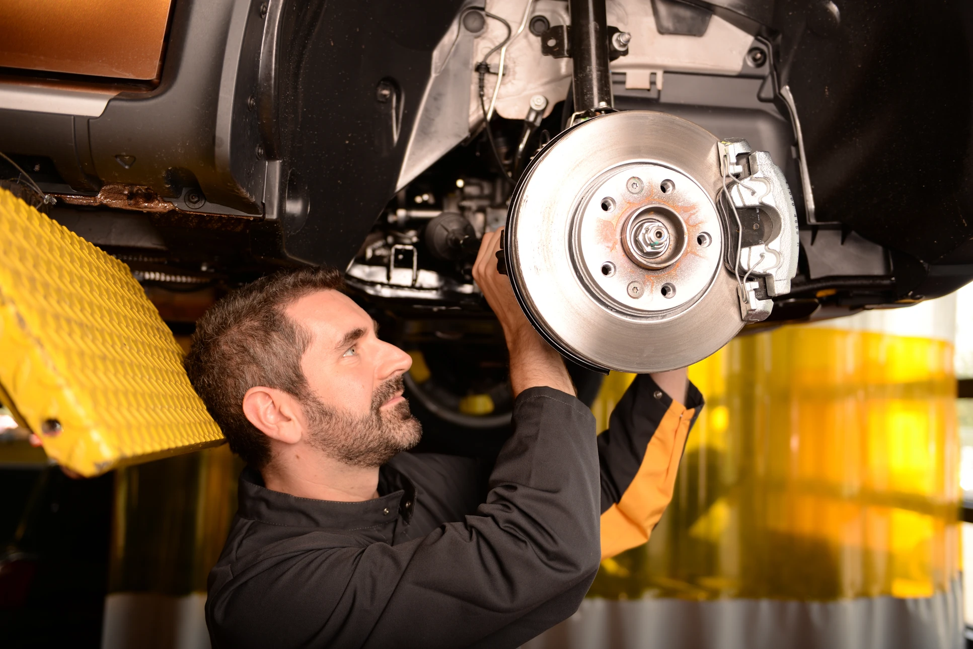 Mécanicien automobile travaillant sous un véhicule surélevé dans un garage professionnel