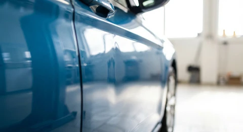 Gros plan sur une carrosserie automobile montrant clairement une bosse ou un enfoncement sur le panneau latéral, en lumière naturelle qui met en évidence le défaut. Le véhicule doit être propre et reconnaissable, la bosse bien visible pour illustrer le problème résolu par le débosselage sans peinture.