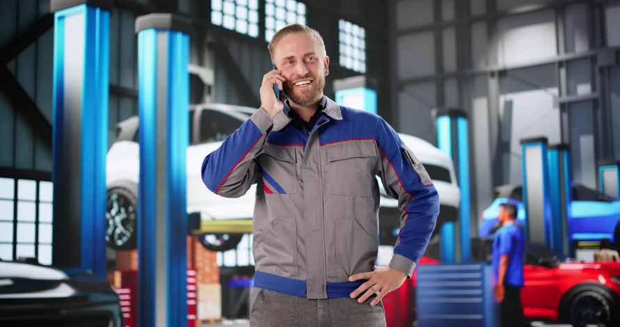 Atelier de carrosserie automobile avec technicien en combinaison de protection intégrale appliquant de la peinture au pistolet sur véhicule gris métallisé